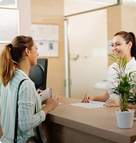A woman interacting with a receptionist at a health facility regarding the waitlist management system.